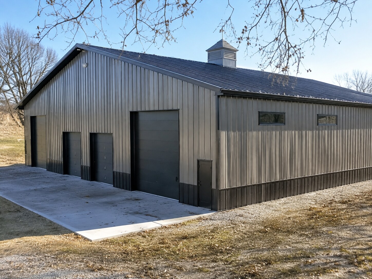 Gray and brown post-frame shop with overhead doors and concrete apron