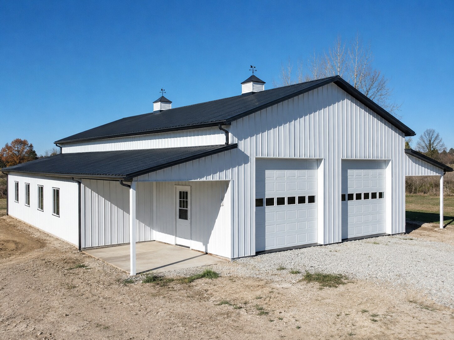 White and gray barn with two overhead doors and roof cupolas