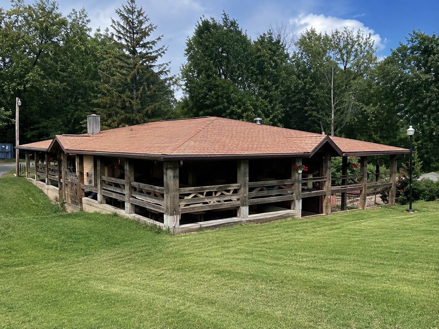 Open-sided timber pavilion with a metal roof in an open yard