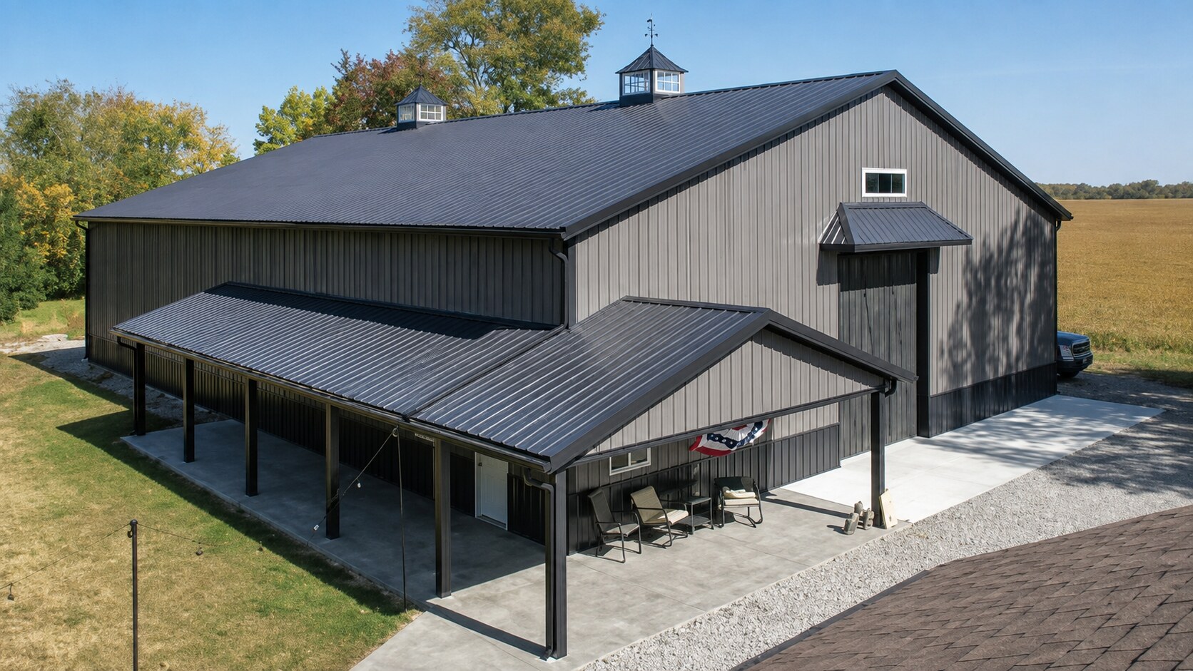 Newly built gray post-frame building with black metal roof and white overhead doors in rural Indiana